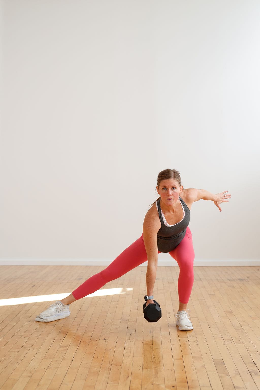 kobieta unosi hantlę nad głowę jedną ręką w pozycji stojącej