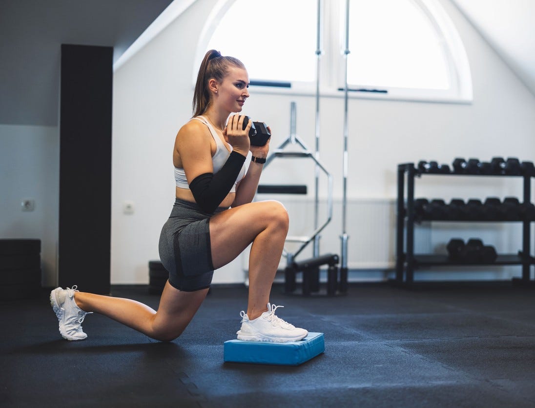 sportowiec stoi na jednej nodze i pochyla się z hantlą w dłoni